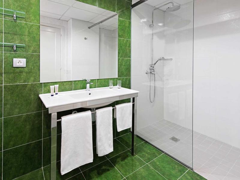 Moderní koupelna se zelenými dlaždicemi, dvojumyvadlem a velkým sprchovým koutem s skleněnou příčkou.