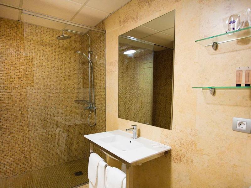 Moderní koupelna se umyvadlem, velkým zrcadlem a sprchovým koutem s mozaikovou stěnou.