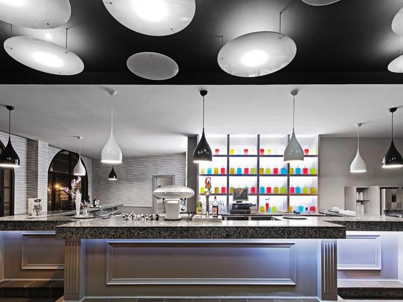 Moderní hotelový bar s barevnými lahvemi a stylovými závěsnými svítidly nad pultem.