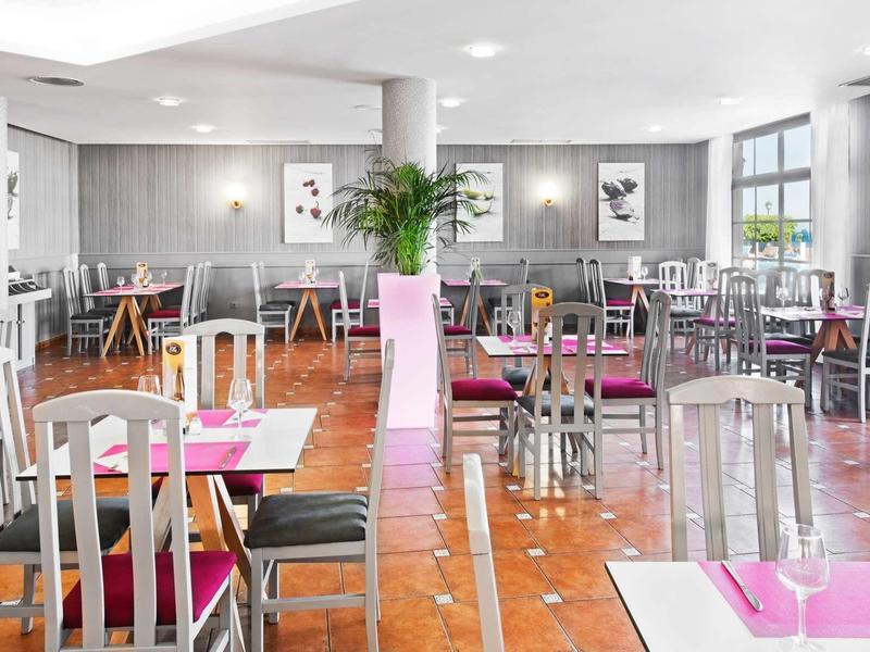 Světlá, moderní restaurace s bílými židlemi a růžovými prostíráními na dlaždicové podlaze.