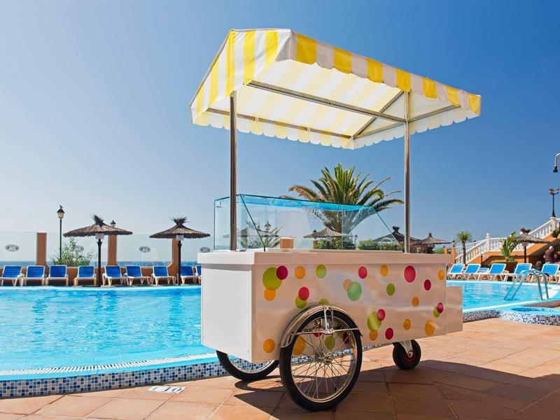 Stánek s ledovou zmrzlinou se žluto-bílým slunečníkem u bazénu v slunečném letovisku