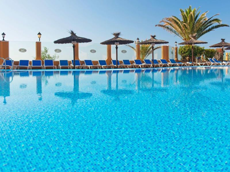 Velký bazén s modrou vodou, lehátky a slámovými slunečníky pod jasnou oblohou