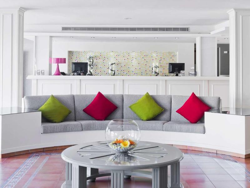 Moderní lounge s velkou pohovkou, barevnými polštáři a kulatým stolem s miskou ovoce.