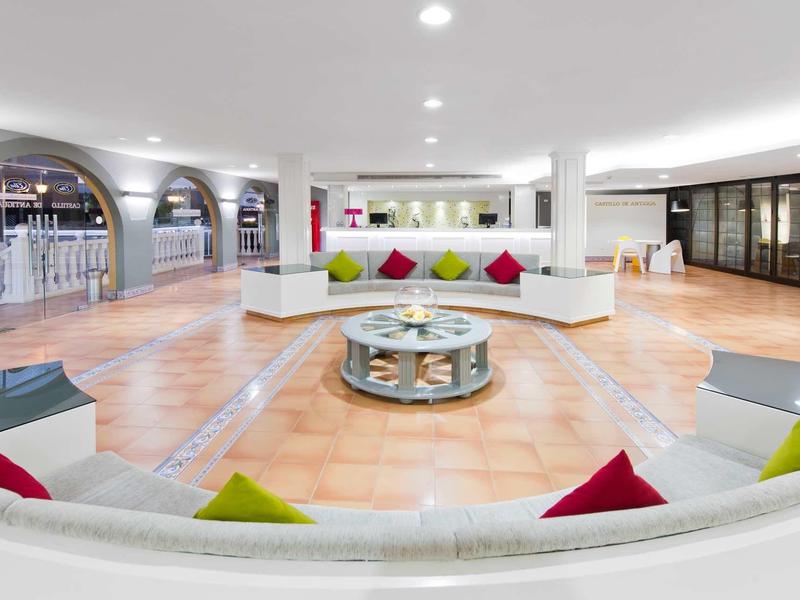 Prostorná hotelová hala s bílými pohovkami a barevnými polštáři na světle hnědé podlaze.