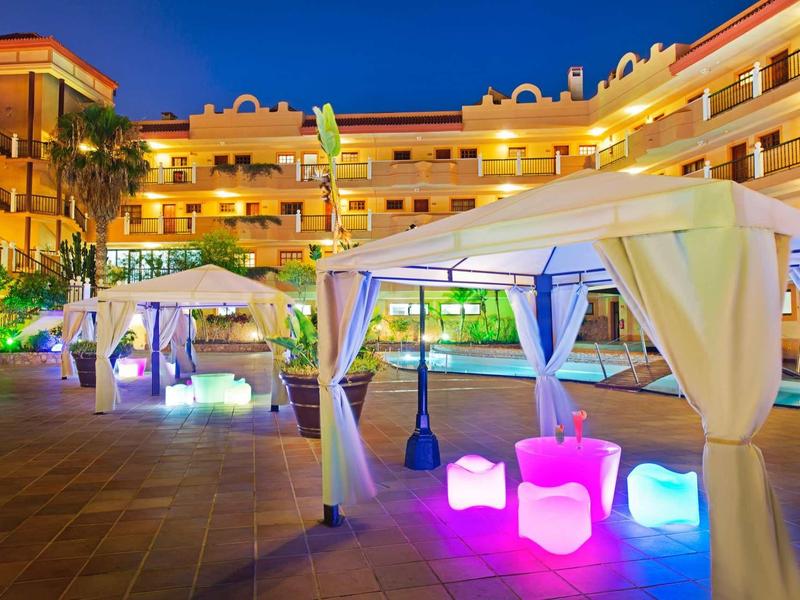 Moderní hotelová terasa s osvětlenými kulatými sedadly a bílými pavilony v noci.