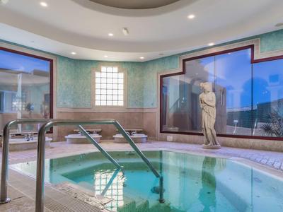 Innenbereich mit rundem Whirlpool, Marmorstatue, großen Fenstern und weichen Deckenlampen.