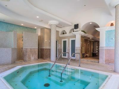 Hell beleuchteter Innenpool mit Treppe, Säulen und blauen Mosaikwänden in modernem Spa-Bereich.