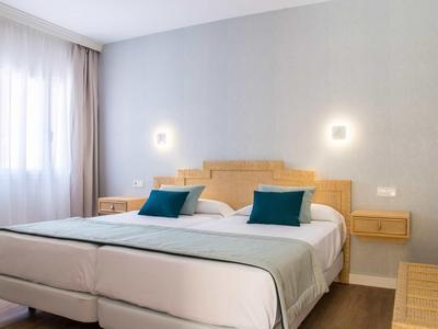Modernes Schlafzimmer mit zwei Einzelbetten, blauem Kissen, Holzmöbeln und hellgrauer Wand.