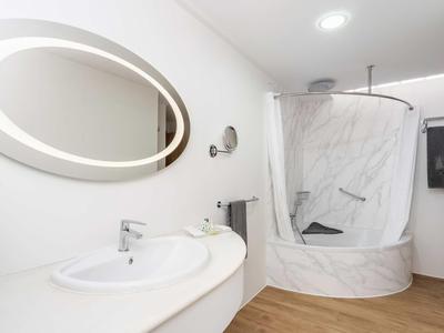Modernes Badezimmer mit rundem Spiegel, Waschbecken, runder Duschkabine und Holzfußboden.
