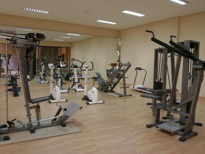 Fitnessraum mit verschiedenen Trainingsgeräten, Holzfußboden und hellen Wänden, gut beleuchtet.
