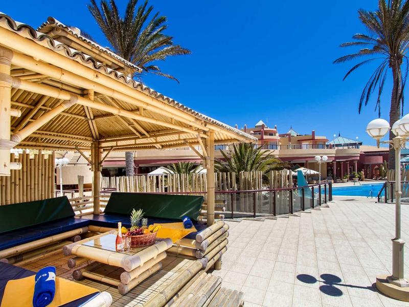 Un elegante lounge sulla spiaggia con posti a sedere coperti circondati da sabbia e palme.