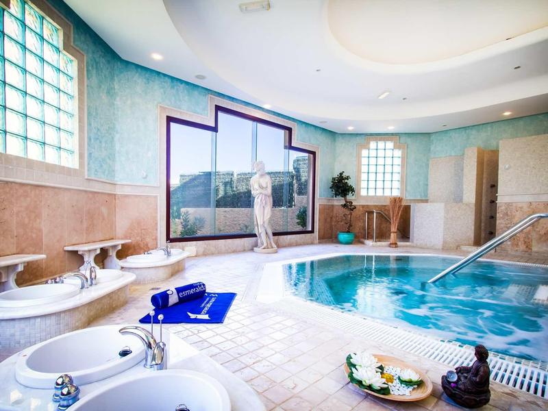 Elegante area benessere con piscina, vasca idromassaggio e statua decorativa in ambiente luminoso.