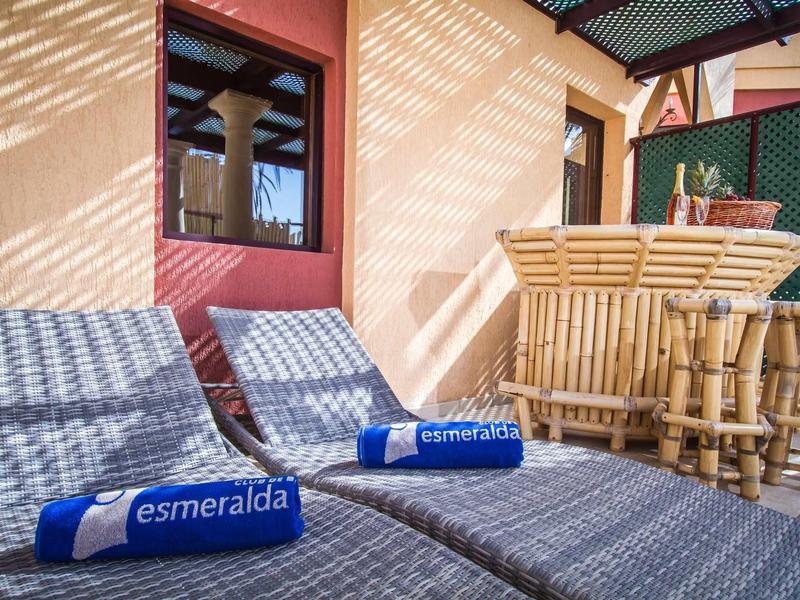 Due chaise a sdraio grigie con asciugamani blu su una terrazza soleggiata accanto a un bar.