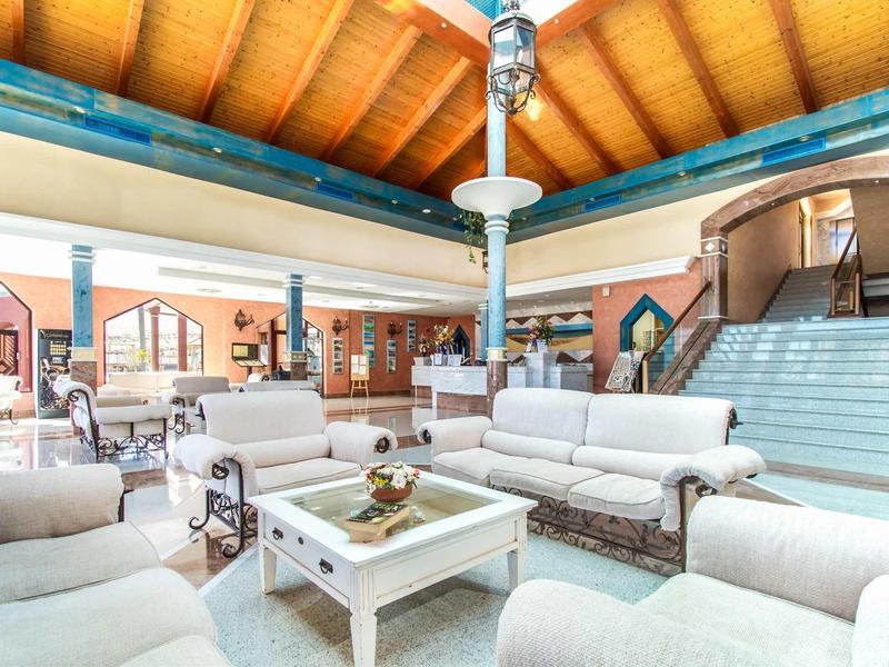 Ampia hall d'hotel con divani bianchi, tavolo in vetro e soffitto in legno con travi a vista.