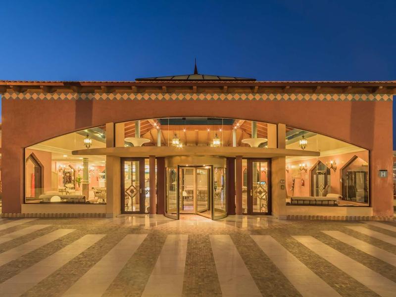 Ingresso di un hotel con area pavimentata ampia e interno illuminato al crepuscolo.