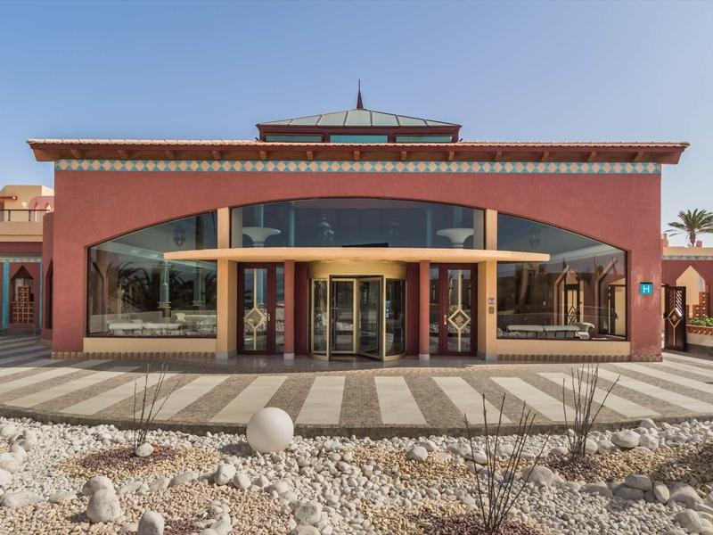 Ingresso dell'hotel con pareti rosse, grandi finestre in vetro e pavimentazione in pietra decorativa.