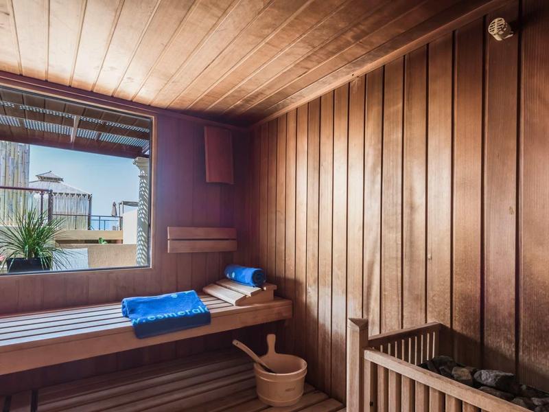 Sauna in legno con panche, finestra e asciugamani blu all'interno.