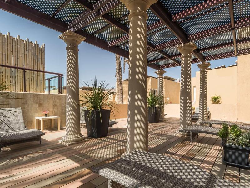 Terrazza coperta con colonne intrecciate e area salotto confortevole in un cortile soleggiato.