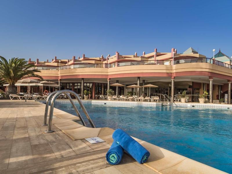 Piscina con asciugamani e edificio dell'hotel sotto un cielo sereno.