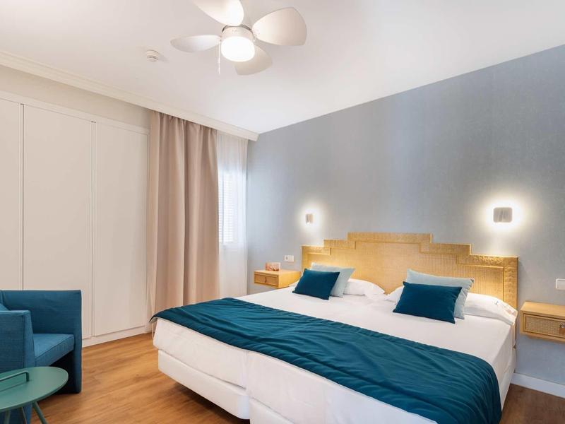 Camera d'hotel moderna con letto matrimoniale, accenti blu e pavimento in legno.