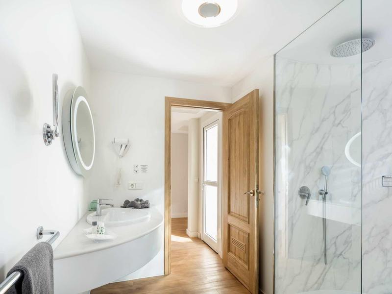 Bagno luminoso con specchio rotondo illuminato, doccia in vetro e porta in legno.