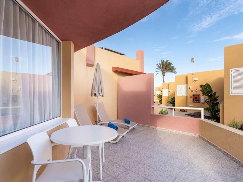 Balcone con tavolo bianco, sedie, sdraio e ombrellone in una giornata di sole.