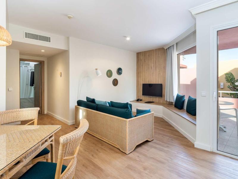 Soggiorno luminoso in appartamento vacanze con divano, tavolo da pranzo, TV e balcone con posti a sedere.