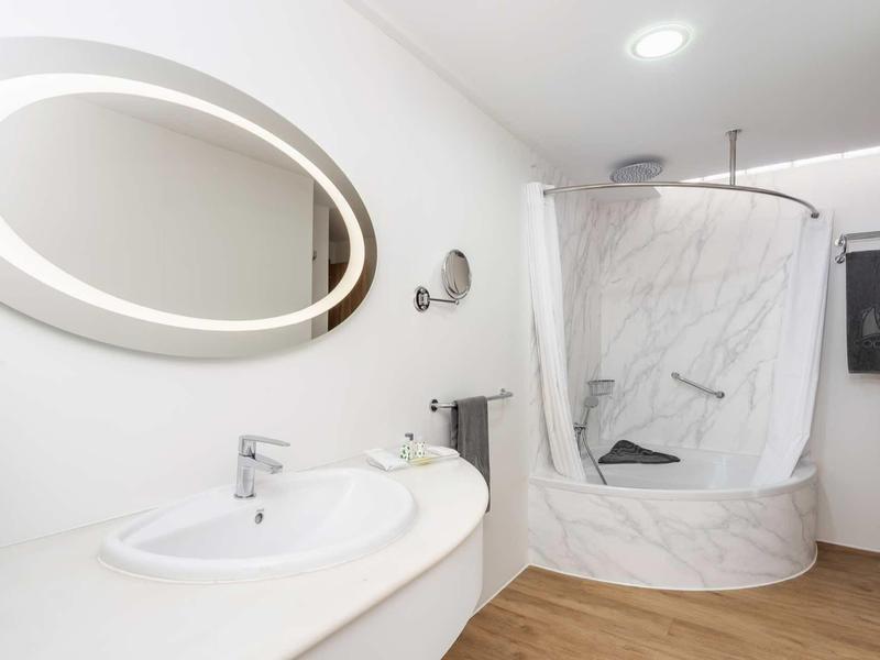 Bagno moderno in hotel con specchio ovale, lavabo e area doccia con tenda.