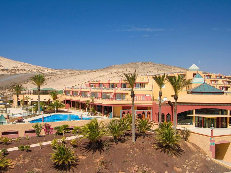 Hotel con piscina e palme in un paesaggio desertico montuoso secco sotto un cielo limpido.