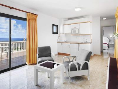 Helles Wohnzimmer mit großem Fenster, weißen Möbeln, grauen Sesseln und gelben Vorhängen.