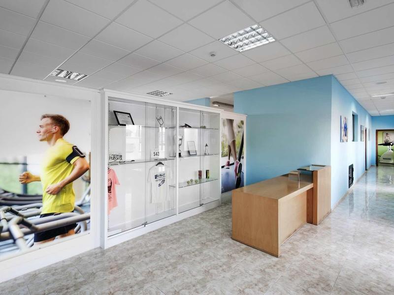 Hell beleuchteter Flur mit blauen Wänden, Holzmöbeln und großen Fitness-Werbeplakaten.