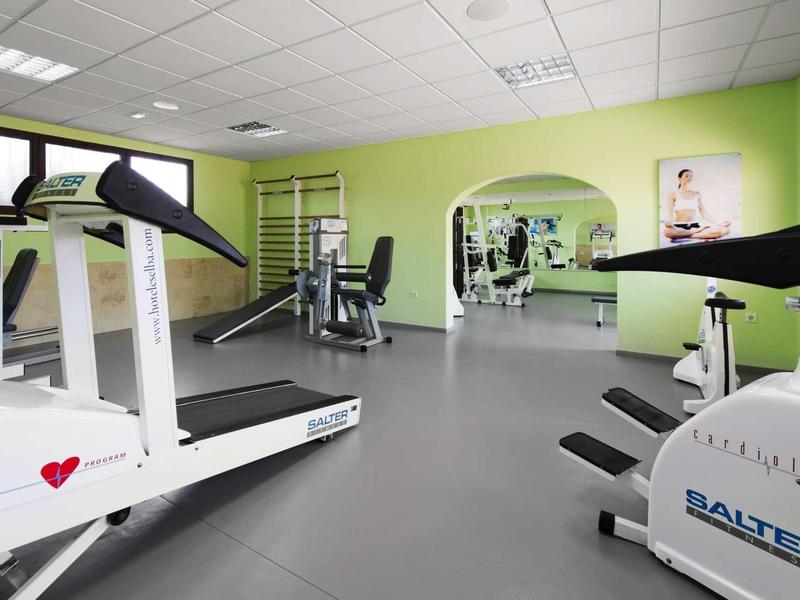 Heller Fitnessraum mit Laufbändern, Fahrradergometer, Kraftgeräten und grün gestrichenen Wänden.