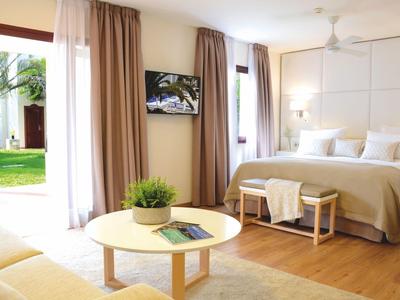 Helles Schlafzimmer mit großem Bett, hellen Vorhängen, runden Tischen und Blick in den grünen Garten.