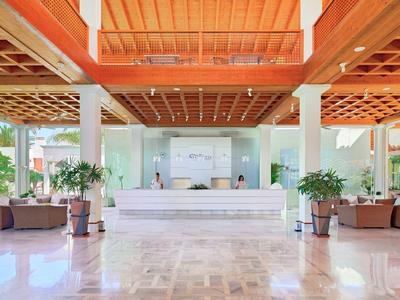 Großer heller Empfangsbereich mit weißer Theke, Holzdecke, grünen Pflanzen und Sitzbereichen.