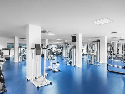 Nowoczesna siłownia z niebieską podłogą, różnymi maszynami do ćwiczeń i jasnym wnętrzem.