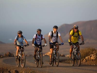 Czterech rowerzystów jedzie po zakurzonej drodze w suchym, górzystym terenie.