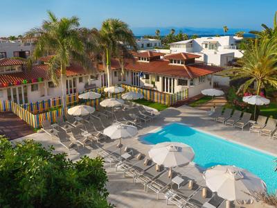 Freizeitbereich mit blauem Pool, weißen Sonnenschirmen und Palmen in sonniger Gartenanlage.