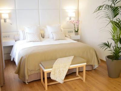 Hell eingerichtetes Schlafzimmer mit großem Bett, zwei Nachttischen und grüner Zimmerpflanze.