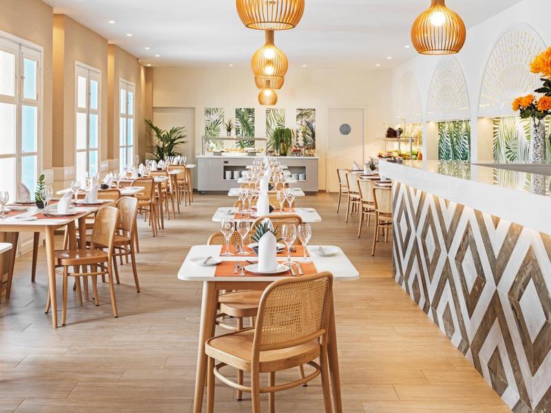 Modernes, helles Restaurant mit Holzmöbeln, geometrischem Tresen und goldenen Pendelleuchten.