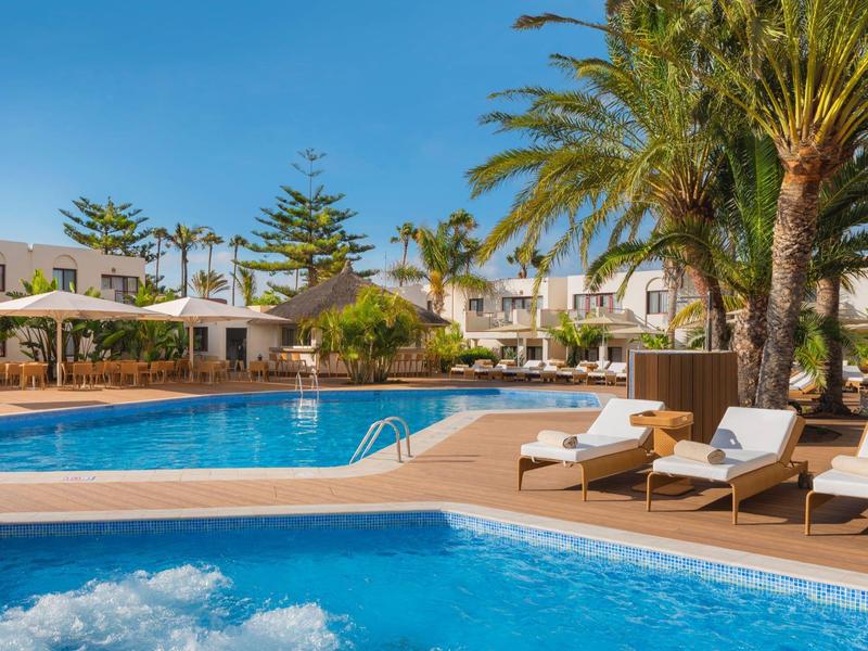 Klare blaue Pools mit Liegestühlen und Palmen in einem sonnigen Resort-Hintergrund.