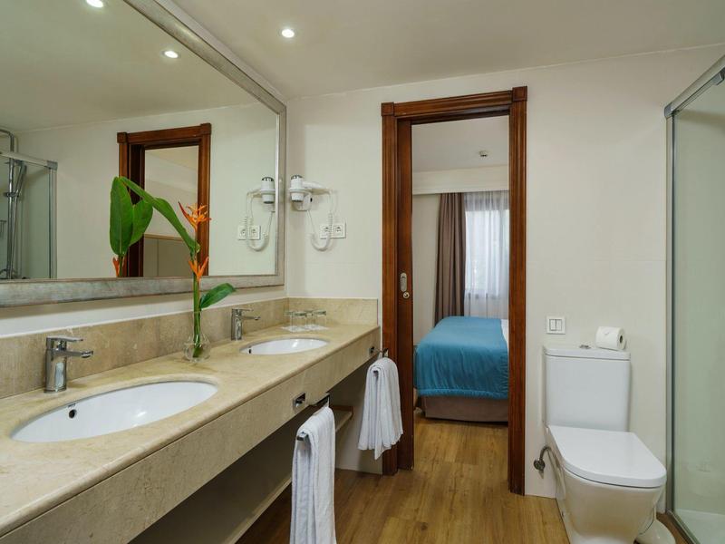 Hell eingerichtetes Badezimmer mit Doppelwaschbecken, großer Spiegel, Dusche und WC, Holzfußboden.