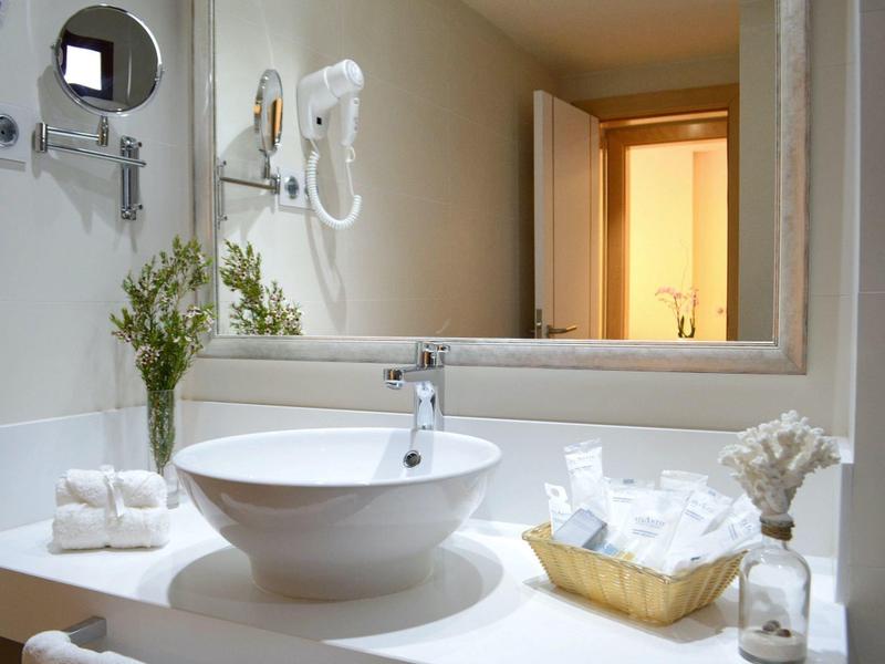 Modernes Badezimmer mit weißem Waschbecken, großem Spiegel und dekorativen Pflanzen.