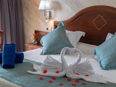 Doppelbett mit weißen und blauen Kissen, Handtücher in Schwanenform und roten Rosenblättern.