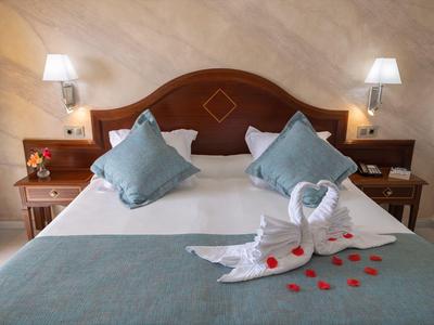 Ein ordentlich gemachtes Bett mit blauen Kissen, zwei Handtuch-Schwanen und roten Rosenblättern.