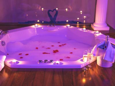 Beleuchteter Whirlpool mit Rosenblättern, Sektgläsern und Kerzen, gemütliche Atmosphäre.