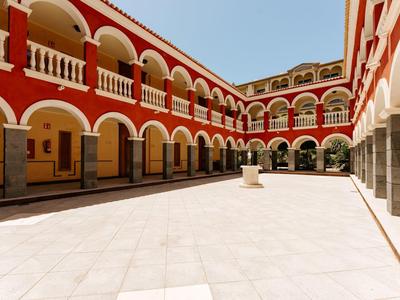 Heller Innenhof mit roten und weißen Arkaden unter klarem blauem Himmel.