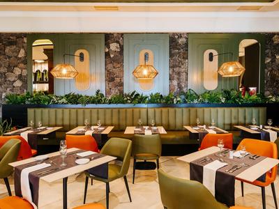 Moderner Restaurantraum mit grünen und orangen Stühlen, Holztischen und hängenden Lampen.