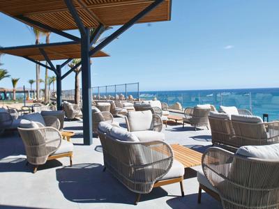 Une terrasse d'hôtel ensoleillée avec des fauteuils en osier face à la mer bleue.