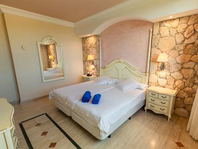 Helles Schlafzimmer mit Doppelbett, Steintapete, Nachttischen, Spiegel und beigen Möbeln.