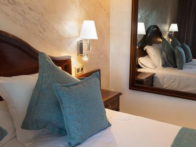 Gemütliches Schlafzimmer mit Bett, blauen Kissen, Wandlampe und großem Wandspiegel.